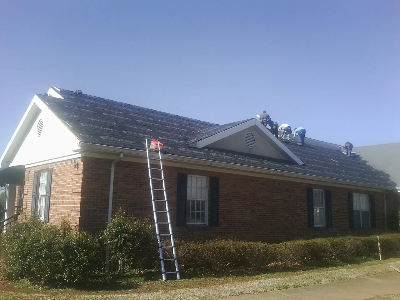 Crew tearing shingles off a brick ranch roof with a ladder set — Emergency Roof Repair work by our crew in Pinetown