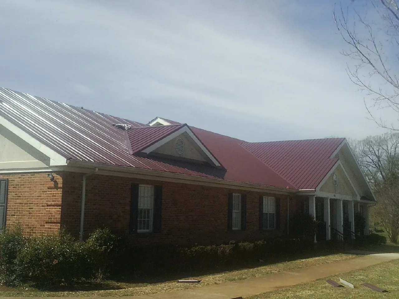 Red metal roof with gabled entries on a long brick building, from a Hail Damage Roof Repair job in Pinetown