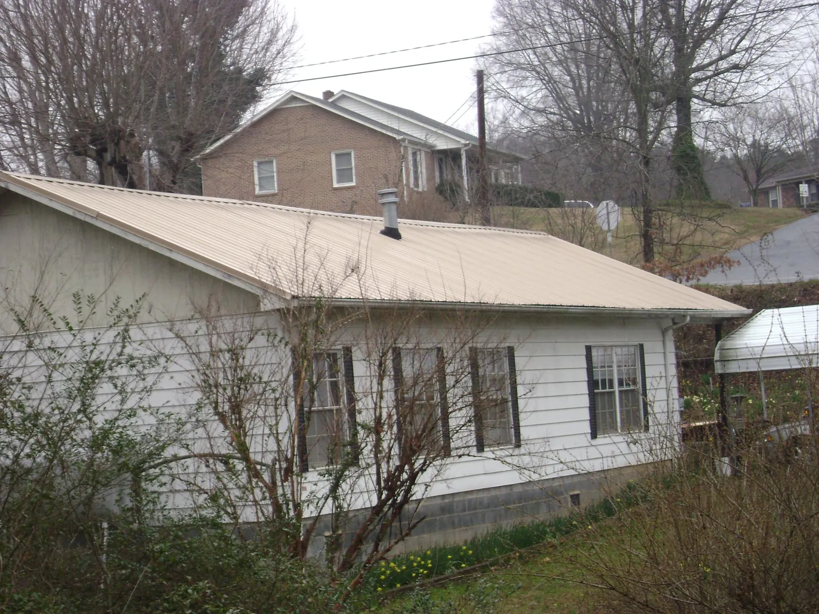 Tan metal roof on a white sided house set into a hillside — Commercial Roofing by Roofing Brothers in Pinetown